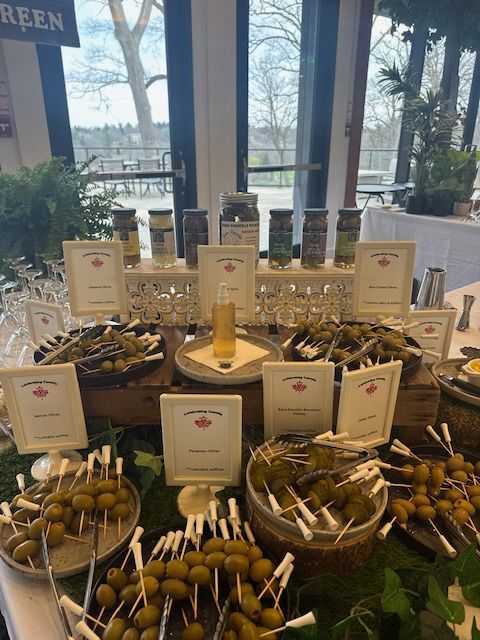 Olive bar with various types of olives on display, with signs and jars of spices.