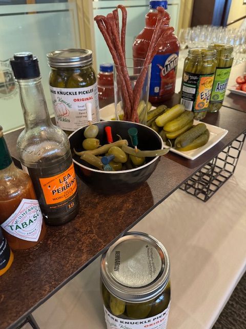 Bloody Mary bar with pickles, meat sticks, olives, hot sauce, and tomato juice.