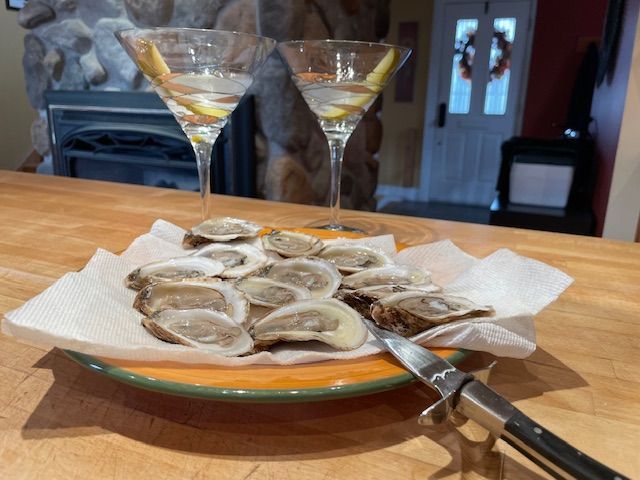 Oysters on a plate with martini glasses in a room with a fireplace, a door, and an oyster knife.