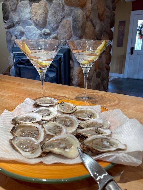Plate of oysters and two martinis on a wooden table, near a stone fireplace.