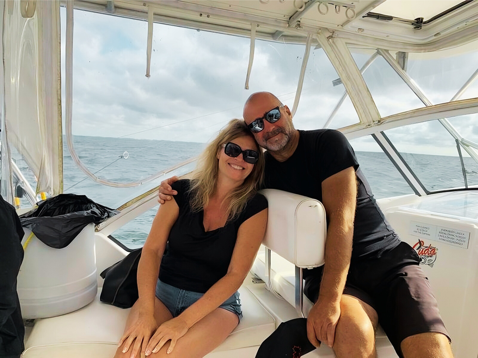 Couple smiles aboard a boat on a cloudy day, man has arm around woman.