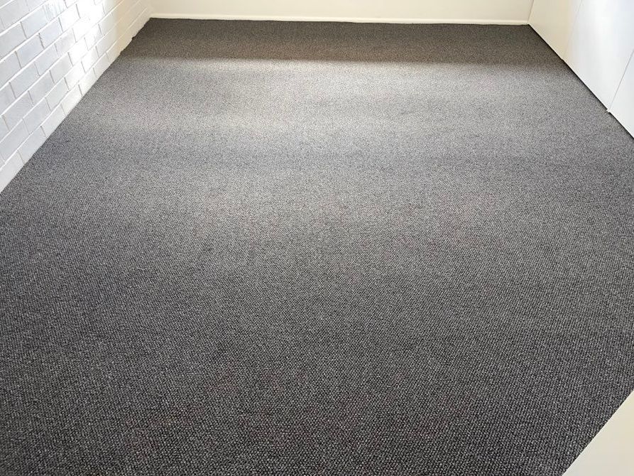 A room with a grey carpeted floor and a white brick wall.