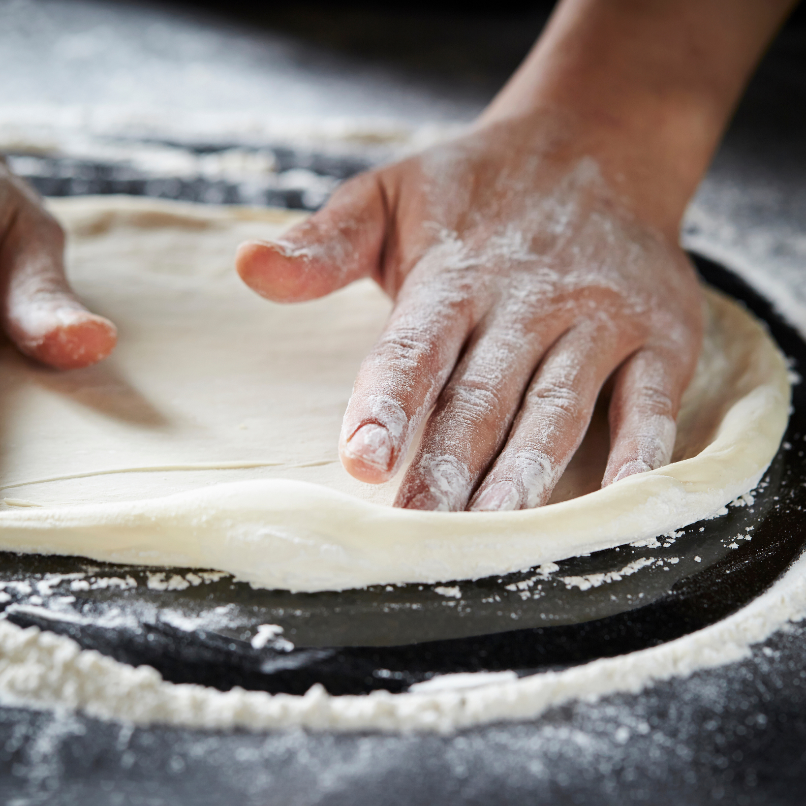 A person 's hands are covered in flour on a pizza dough