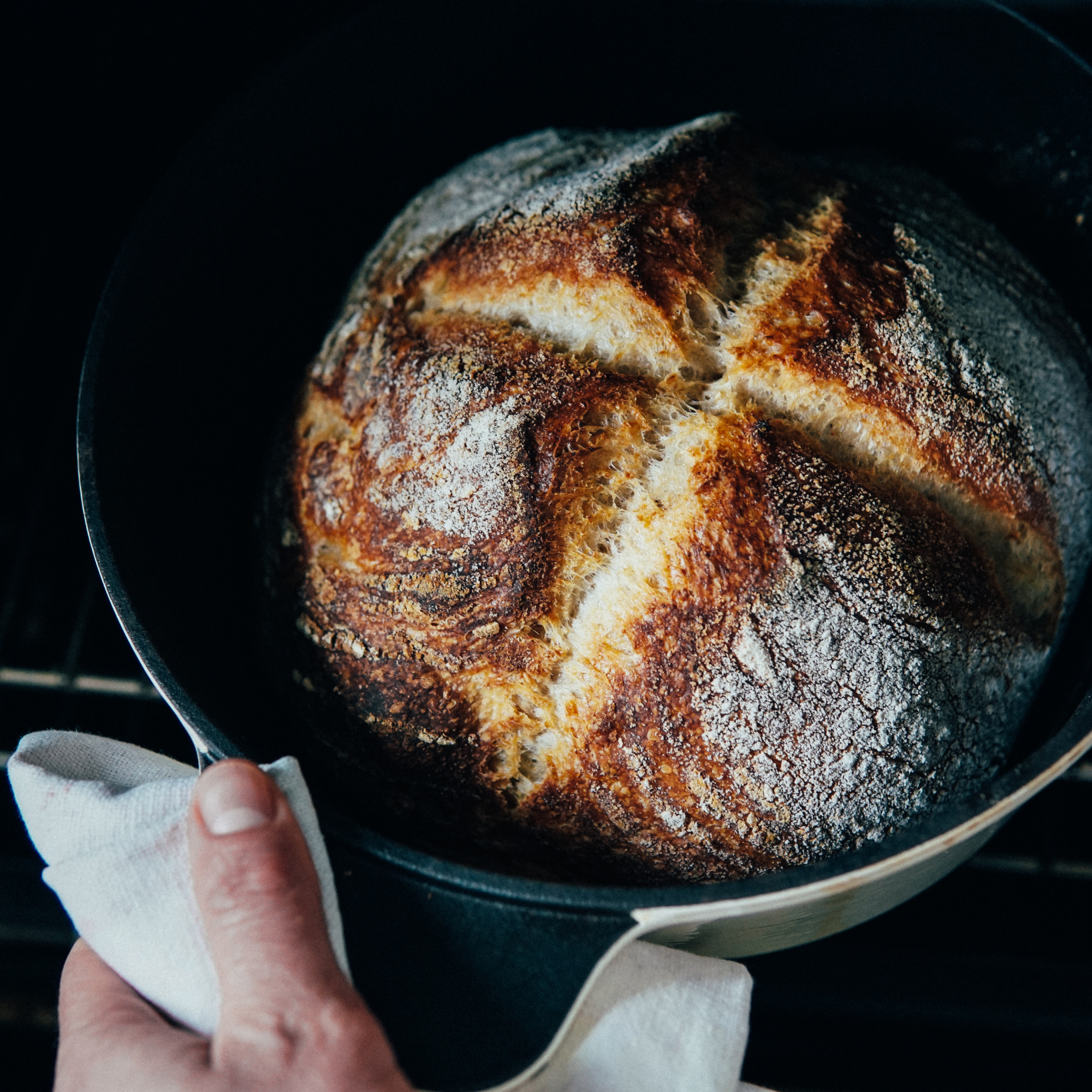 A person is holding a towel over a loaf of bread in a pot.