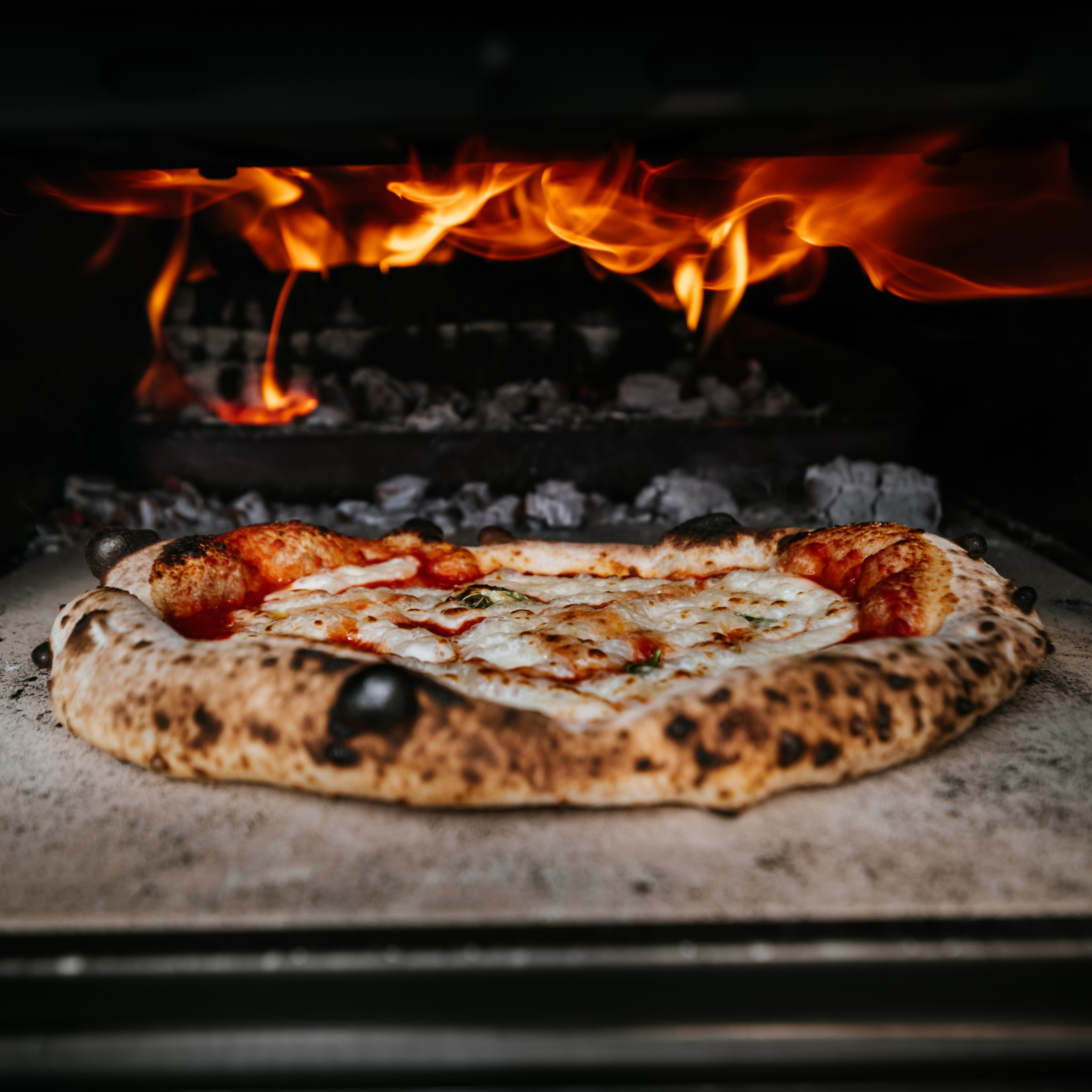 A pizza is being cooked in an oven with flames coming out of it.