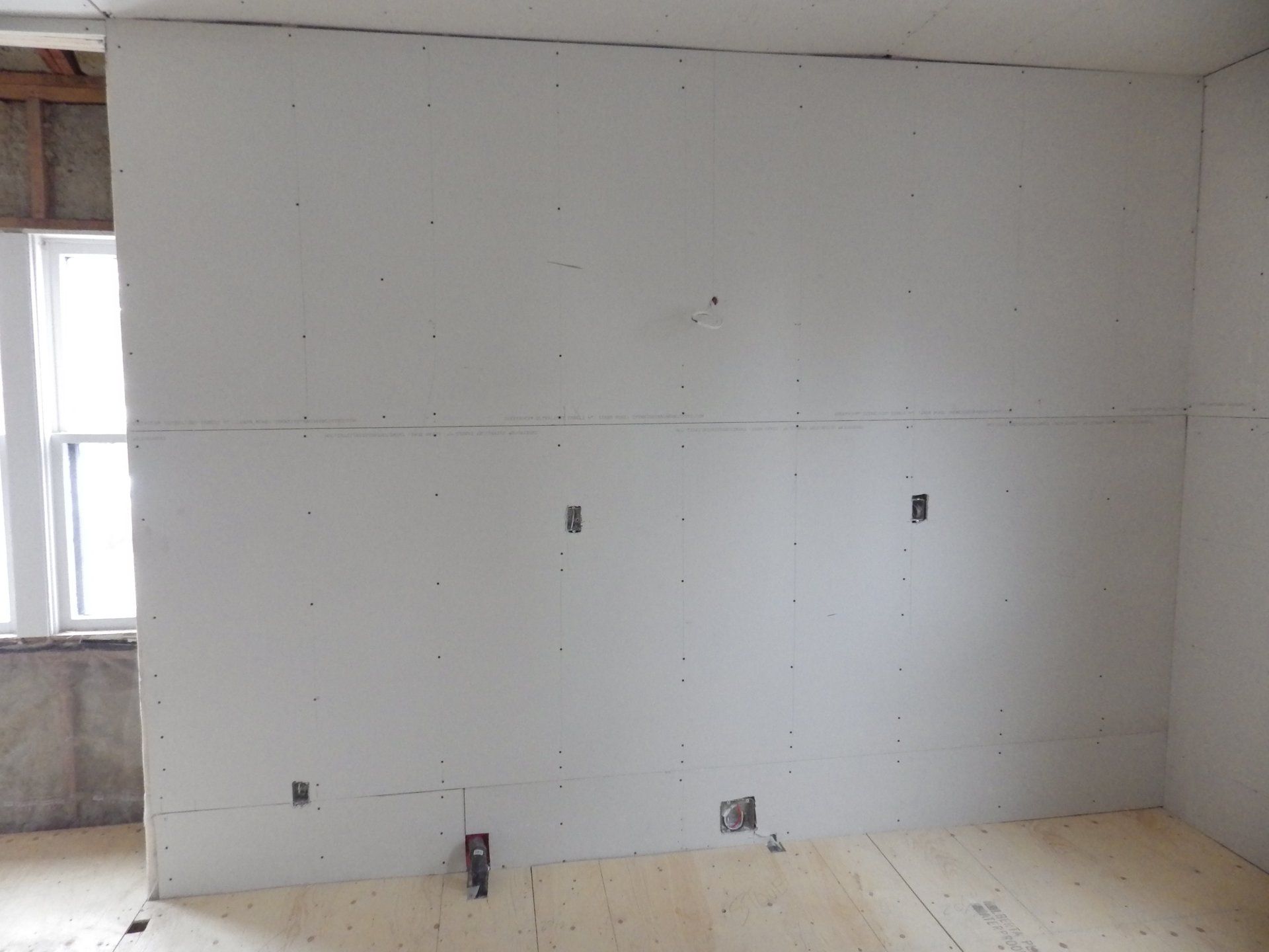 renovation of kitchen looking at unfinished drywall with plugs in walls.