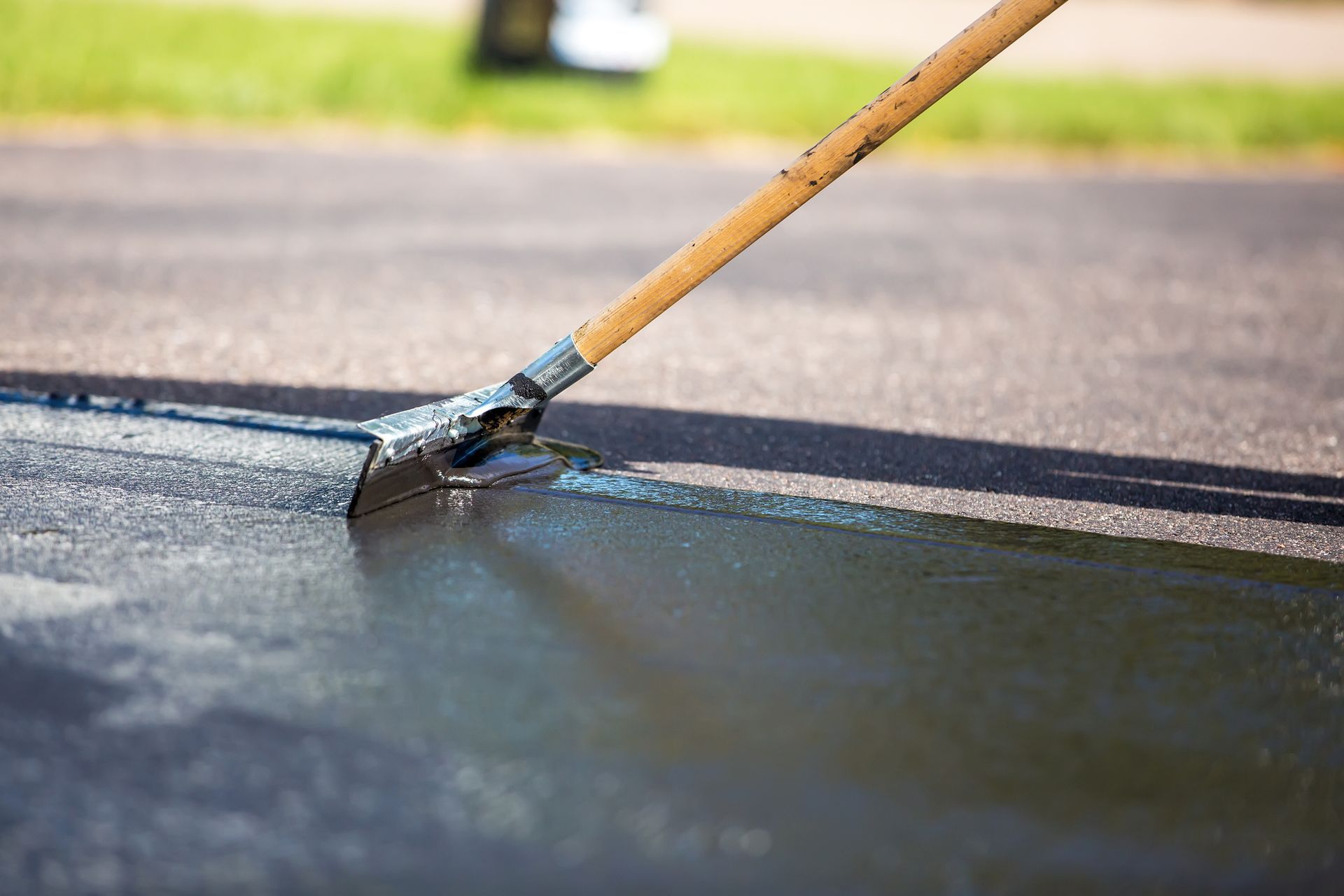 Contractor applying asphalt sealcoat to driveway pavement with squeegee tool.