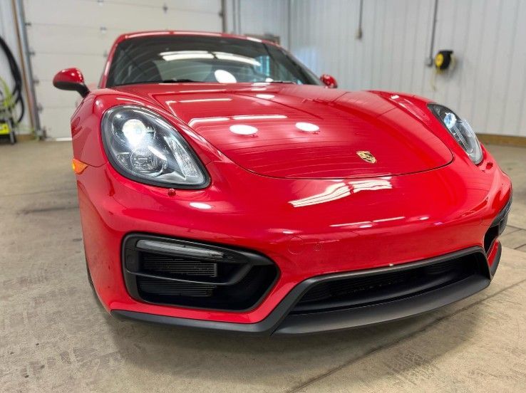 A front-facing, eye-level shot of a glossy red Porsche sports car parked inside a brightly lit garage.