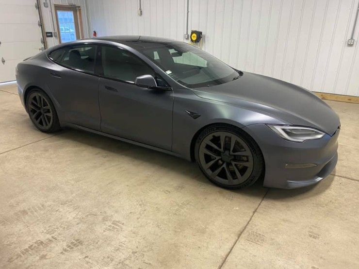 A dark grey Tesla Model S sedan parked inside a garage with concrete flooring.