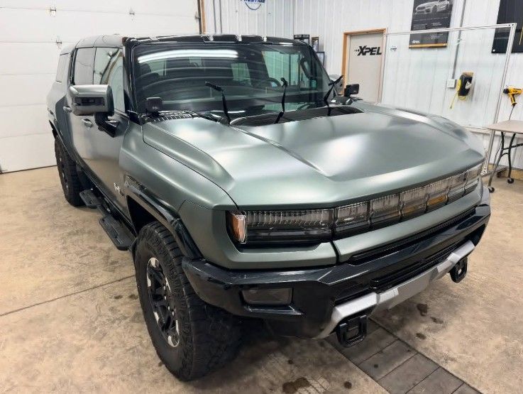 A matte-green Hummer EV SUV parked inside a garage.