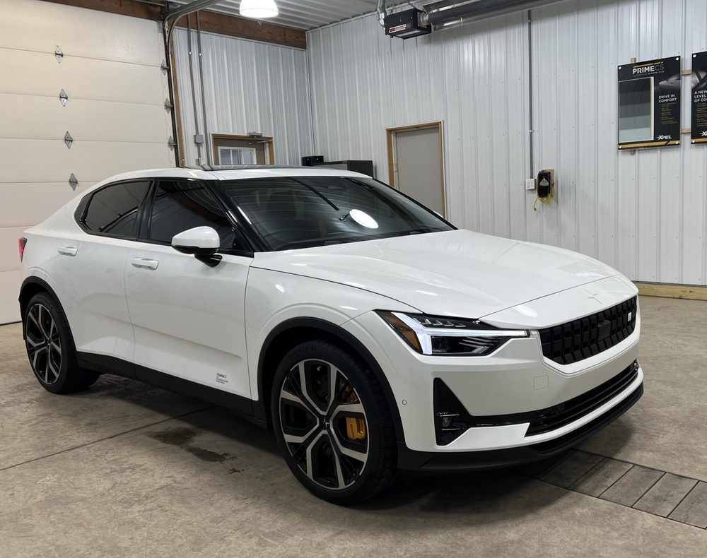 White Polestar 2 electric vehicle, parked in a garage. Black wheels, yellow brake calipers visible.