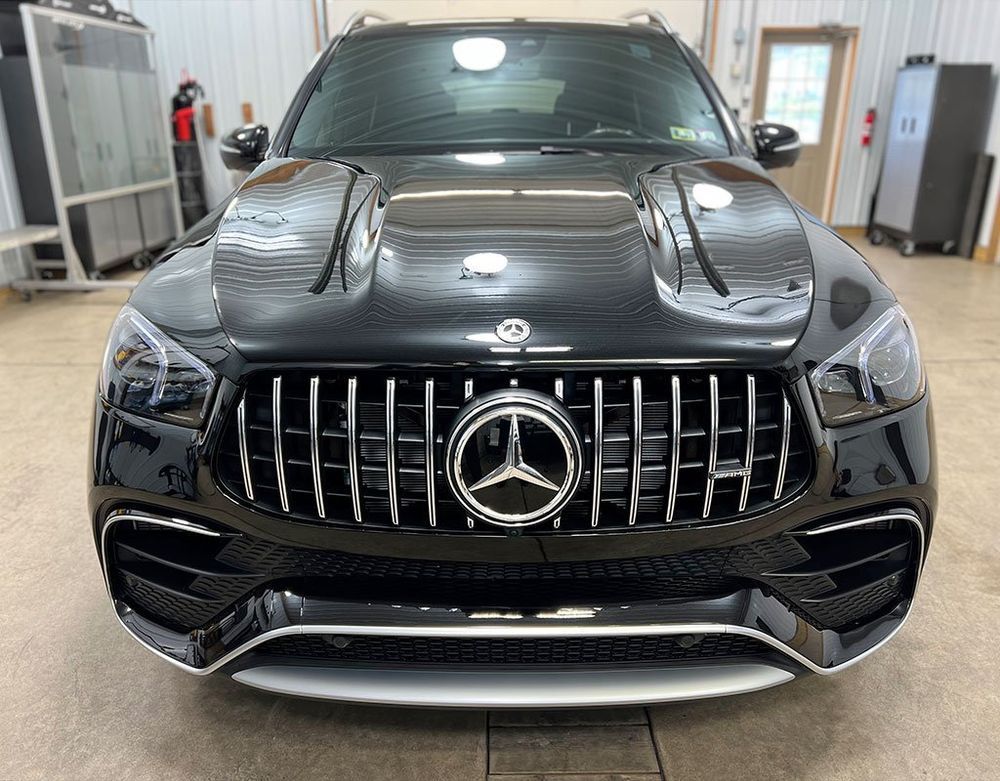 Black Mercedes-AMG SUV, front view, shiny grill, silver emblem, hood vents, indoor setting.