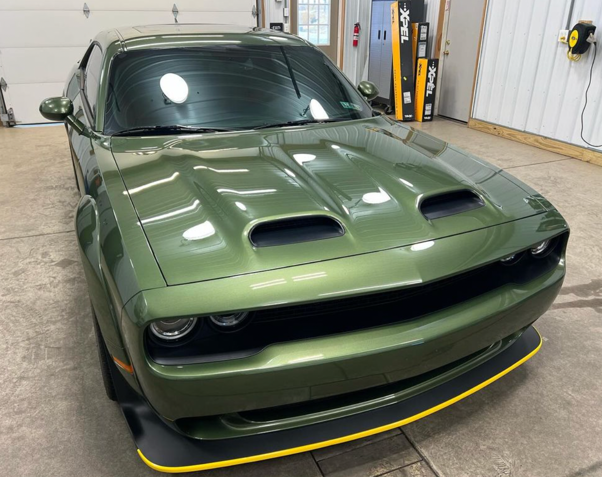 Green Dodge Challenger muscle car with hood scoops in a garage setting.