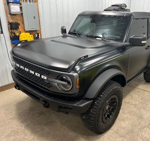 A matte black Ford Bronco SUV parked in a garage with industrial equipment in the background.