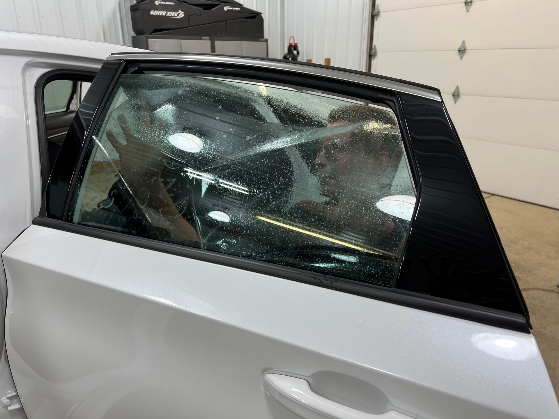 White car door with tinted window film being applied by a person inside.