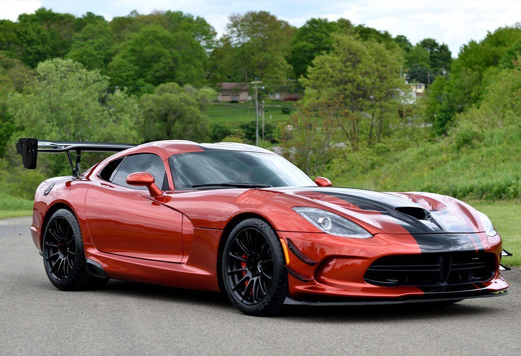Orange and black Dodge Viper sports car on a road, with a black spoiler, trees in the background.