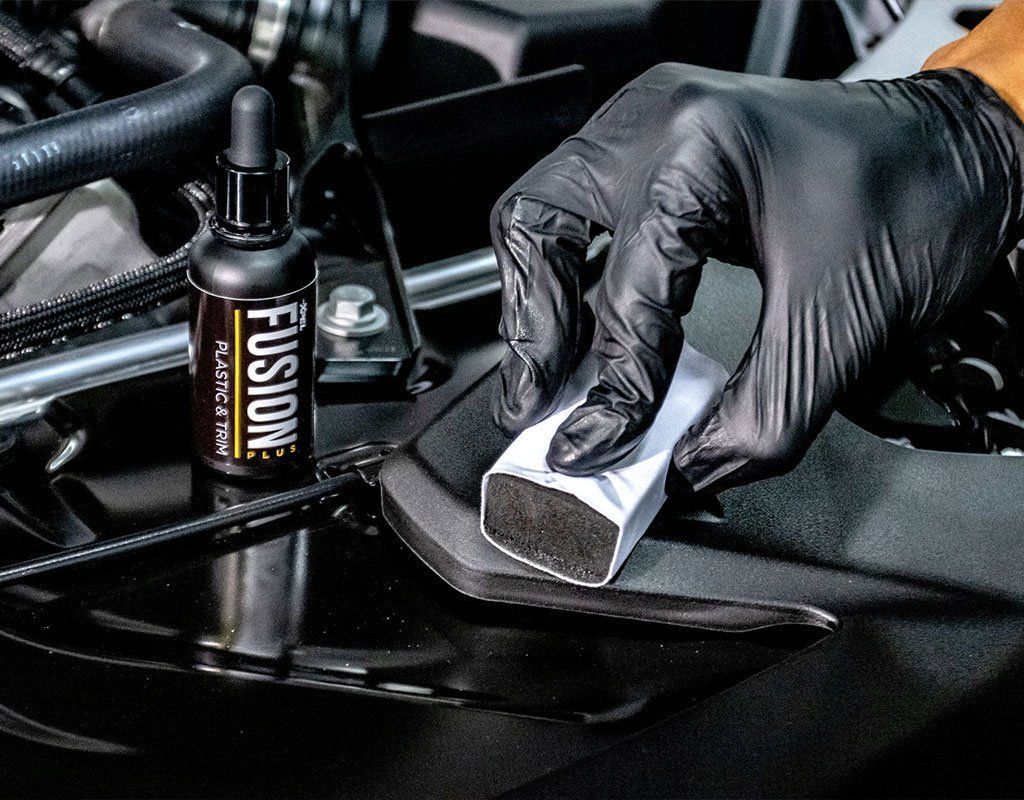Gloved hand applying ceramic coating to car surface with applicator. Product bottle visible.
