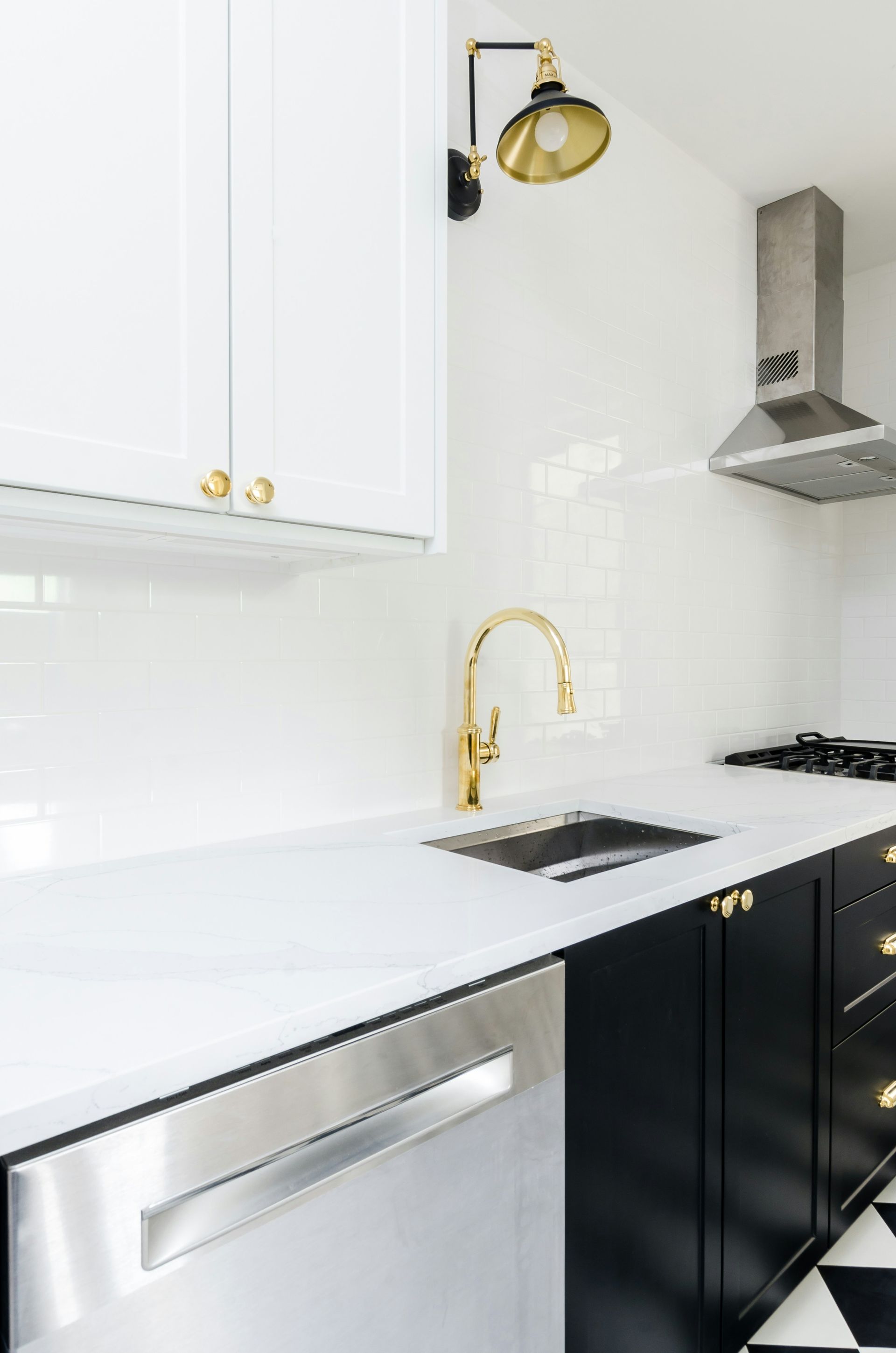 Modern kitchen with white and black cabinets, gold accents, stainless steel appliances, and a tiled backsplash.