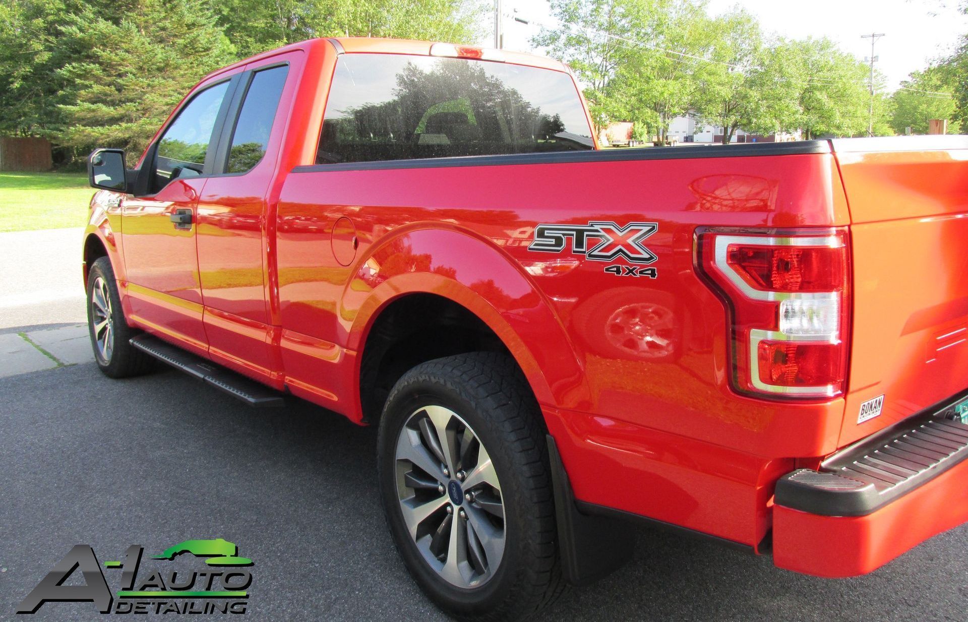 A red ford f150 truck is parked on the side of the road.