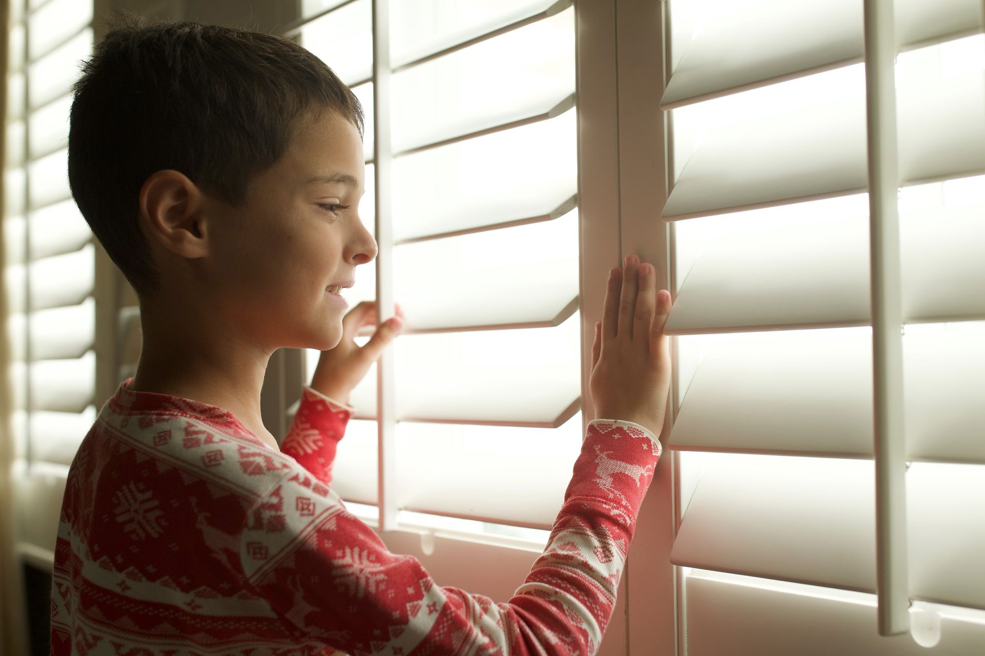 A child standiA child standing near a set of interior shutters ng near a set of interior shutters