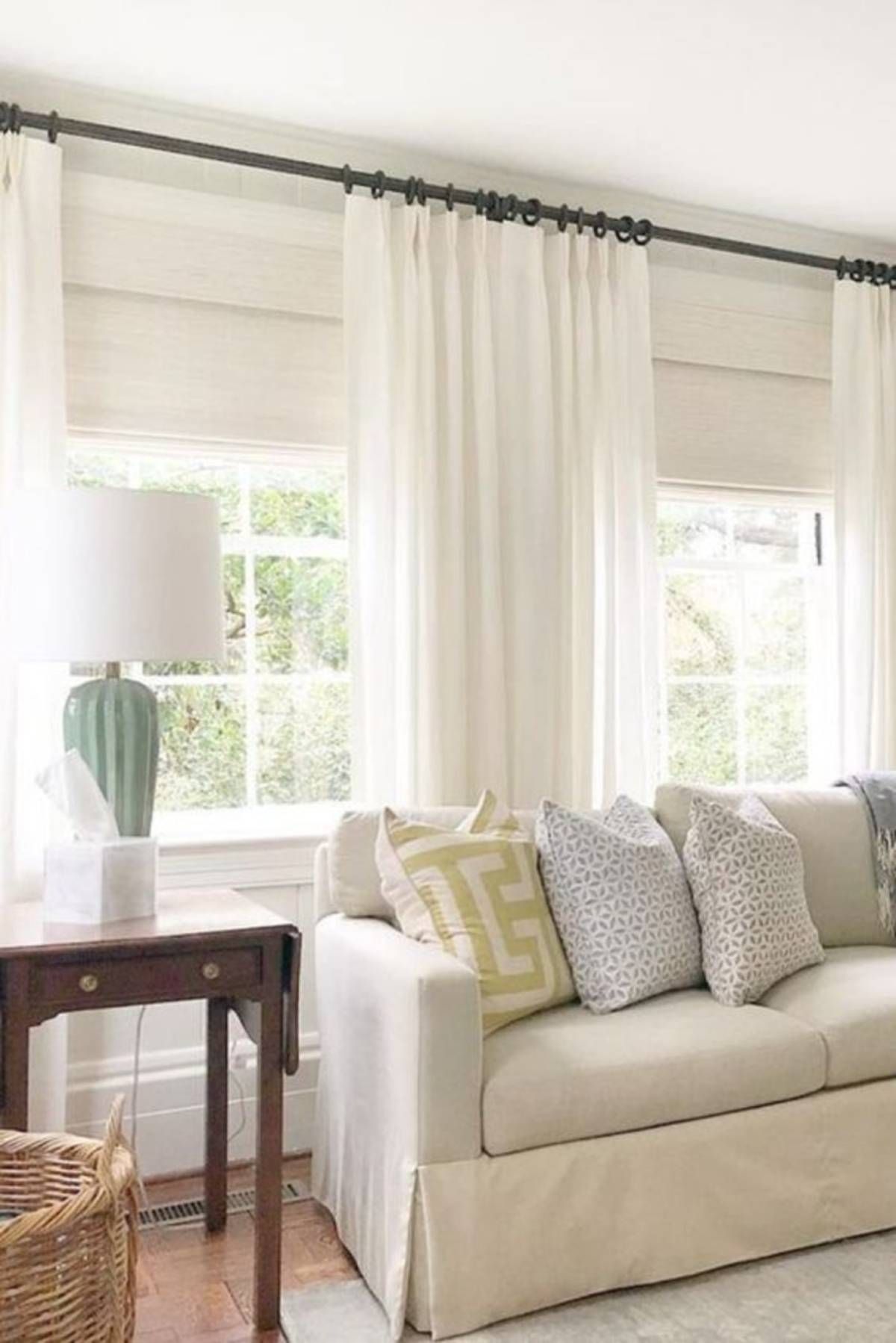 Living room windows with Provenance® woven wood shades layered under sheer white drapery panels as a stylish curtain alternative.
