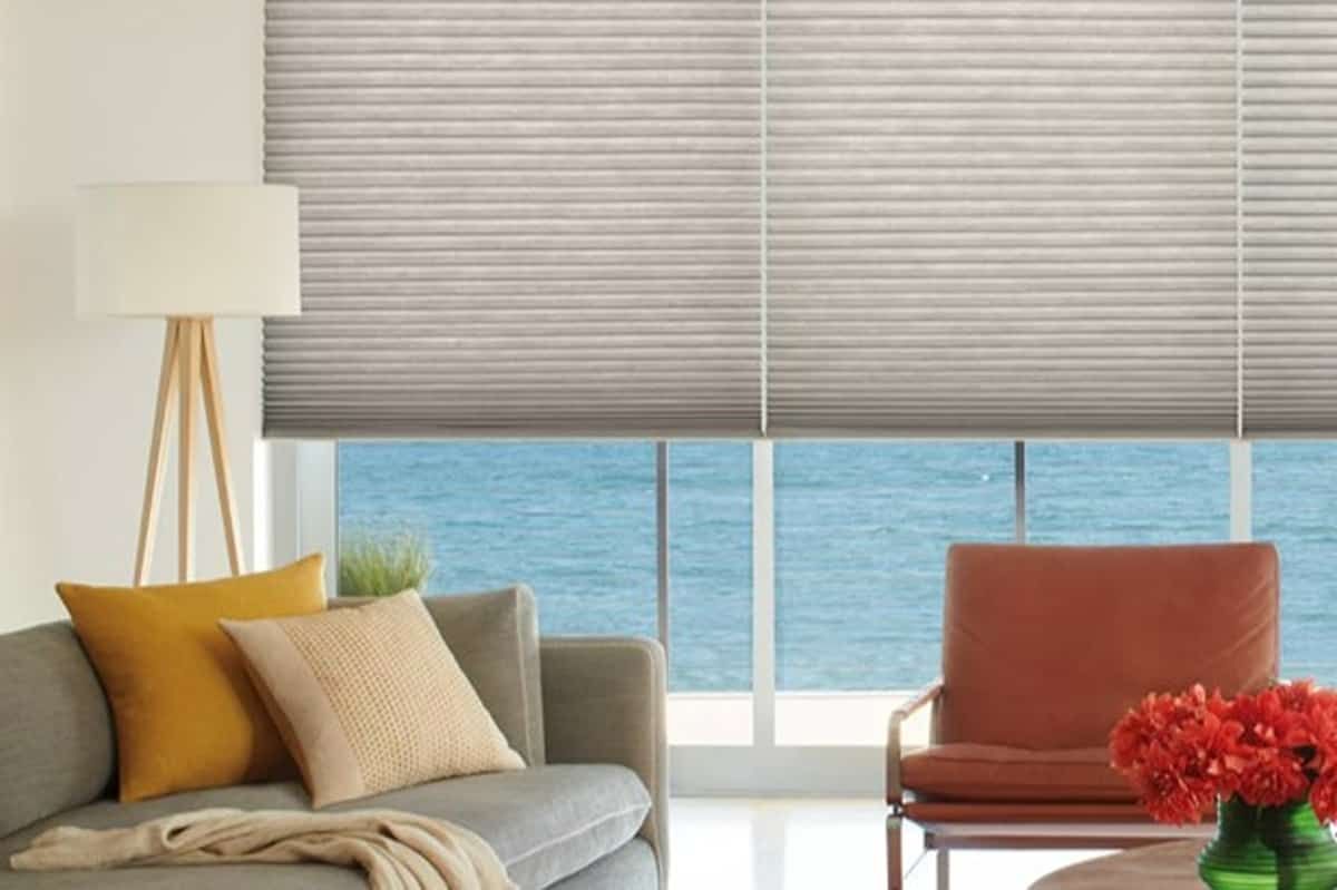 A gray couch and red chair in front of half-drawn Hunter Douglas Duette® Cellular Shades