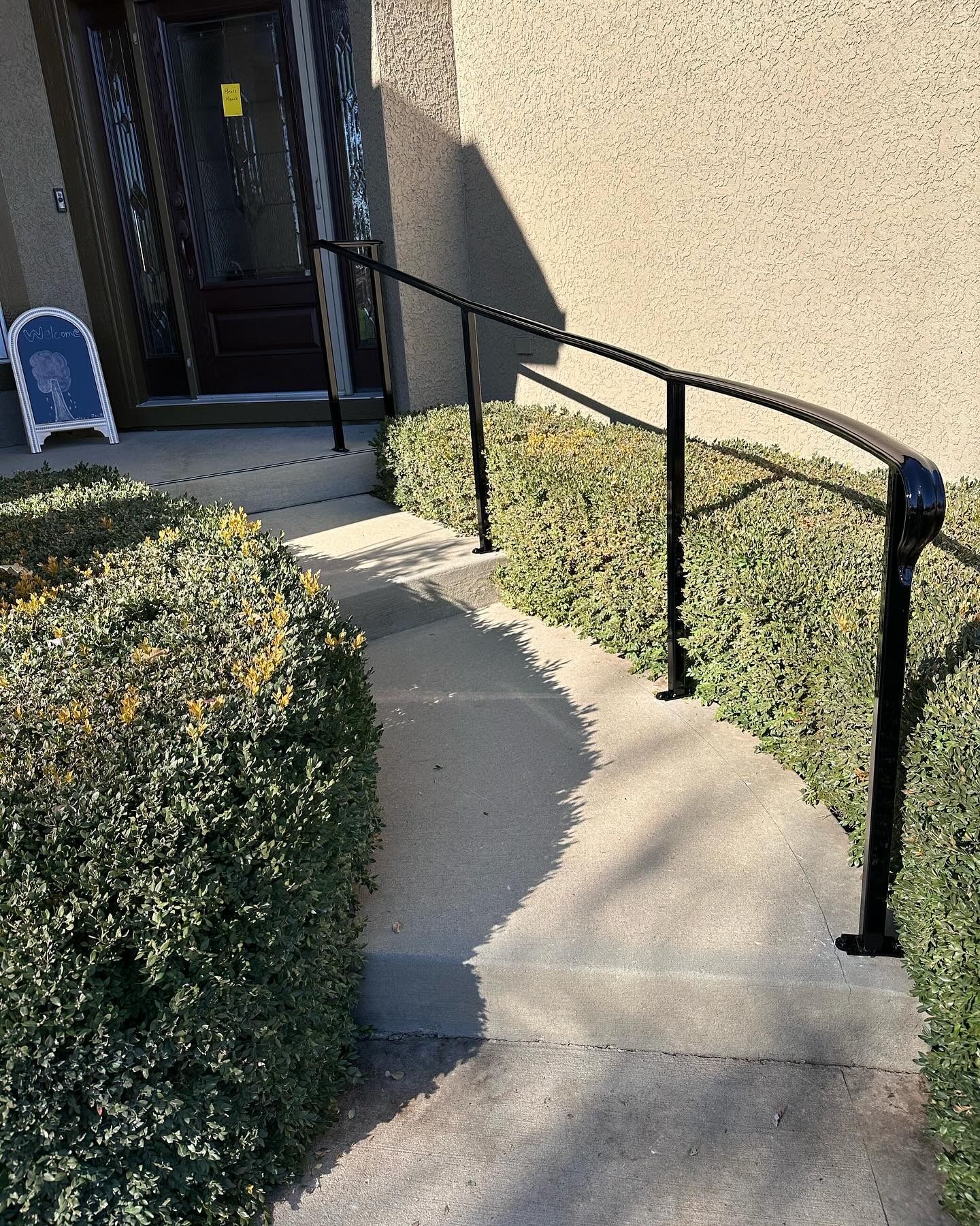 Black metal handrail curves along a concrete path leading to a building entrance.