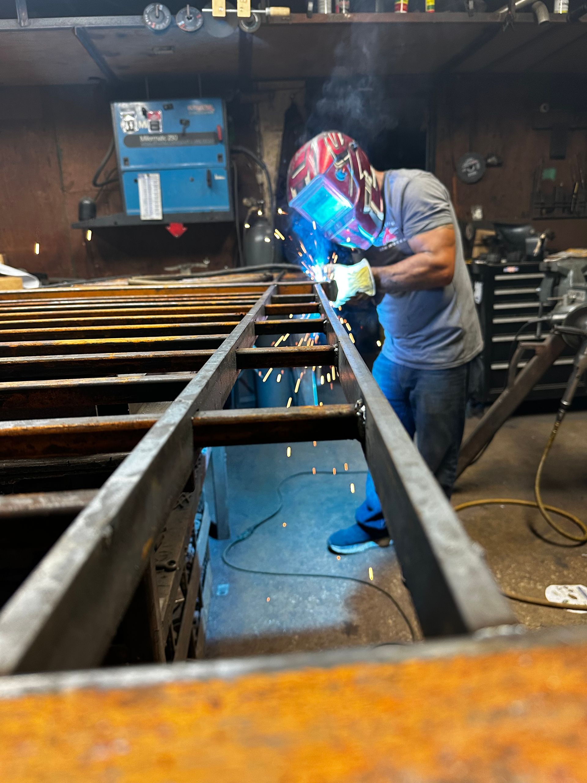 Welder in protective gear welds metal frame in workshop, sparks flying, blue light.