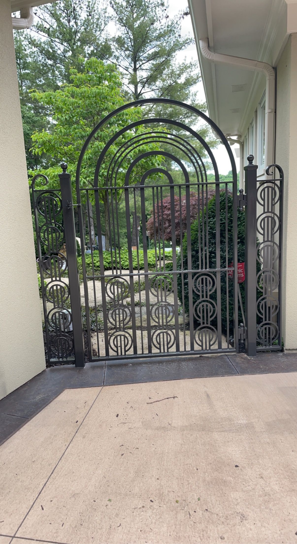 Black metal garden gate with arched trellis leading to a garden path.