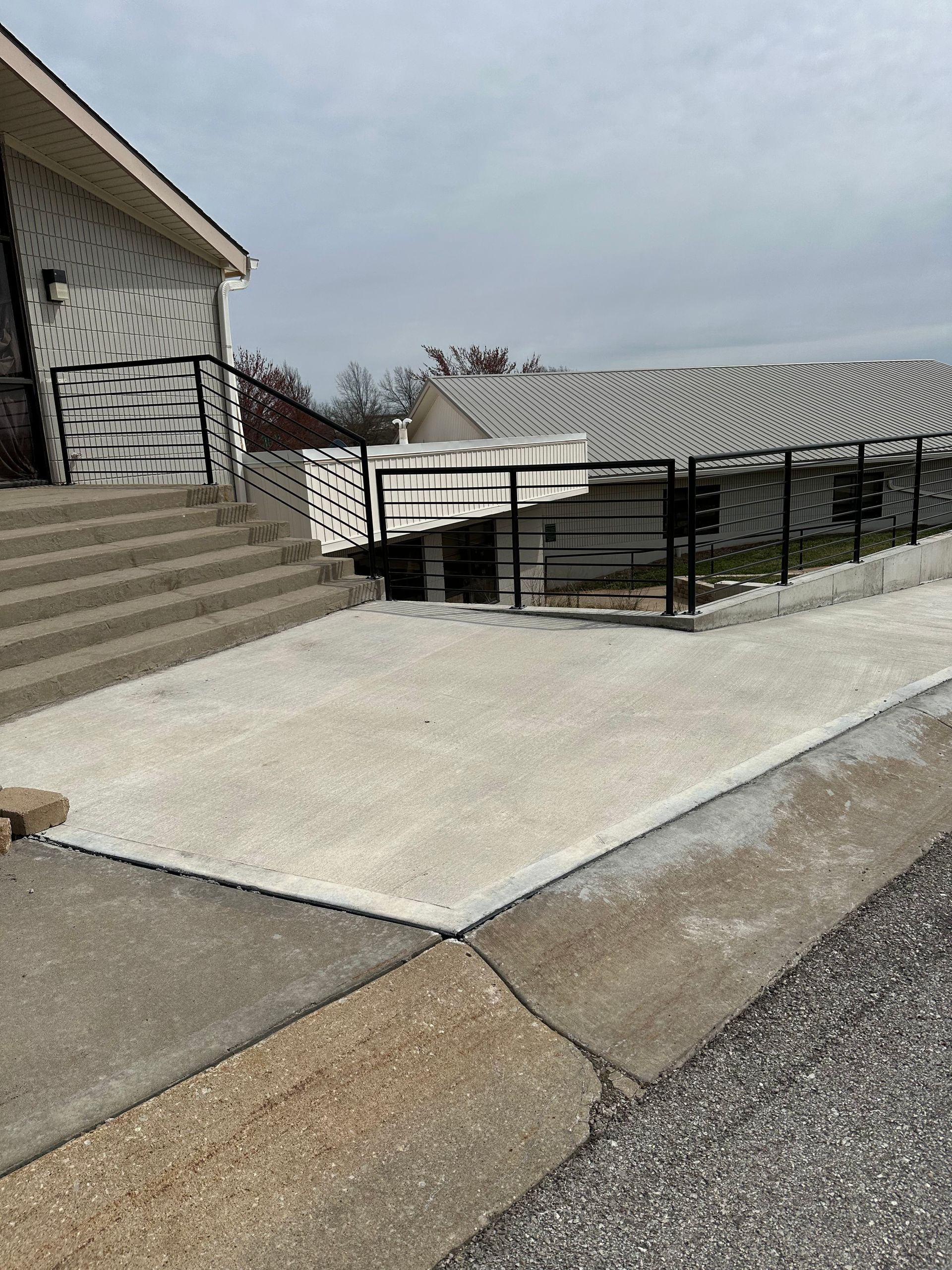 Concrete ramp and stairs leading to a building with black railing on a cloudy day.