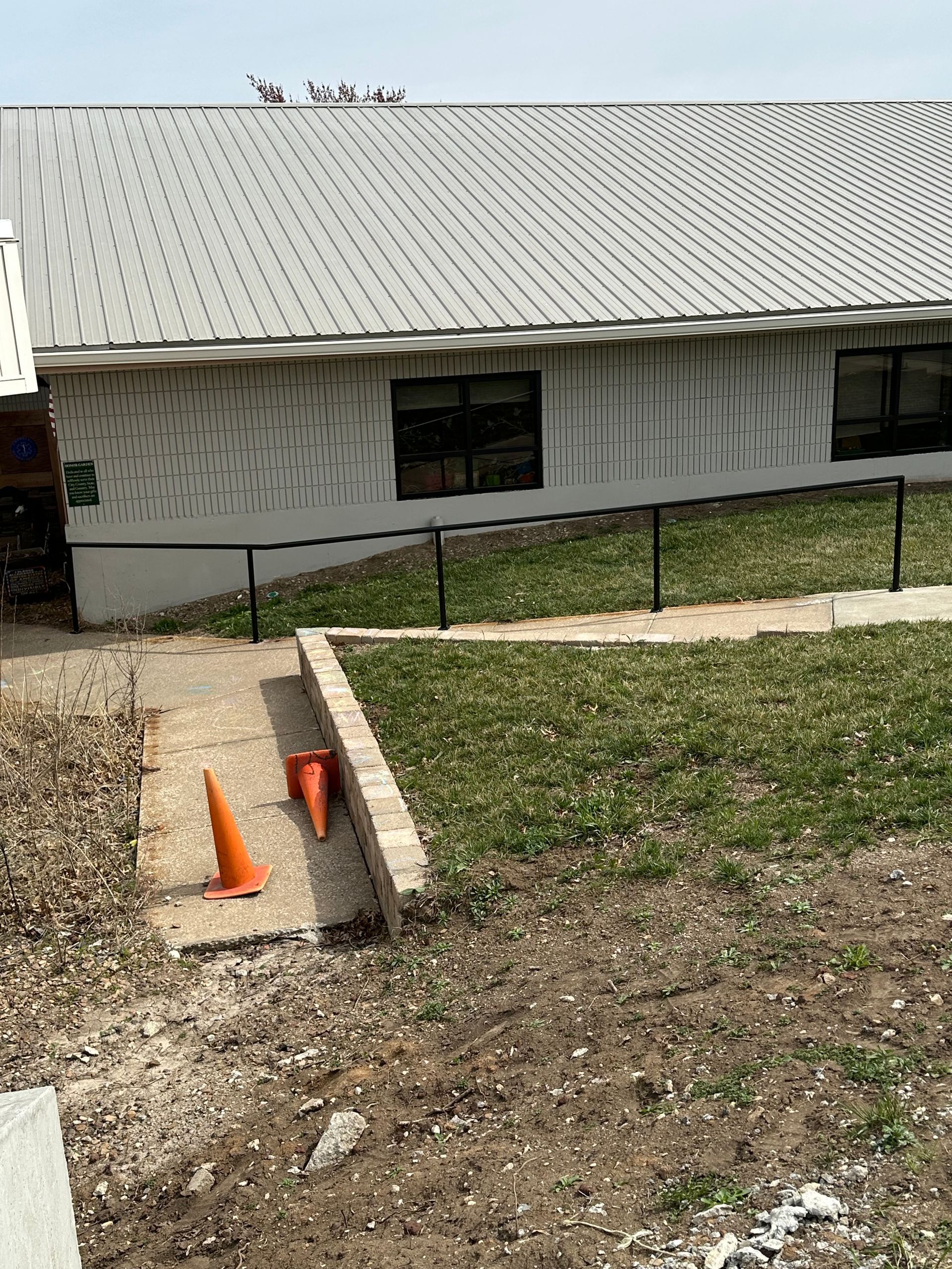 Building with a ramp and handrail; orange cones on pathway.