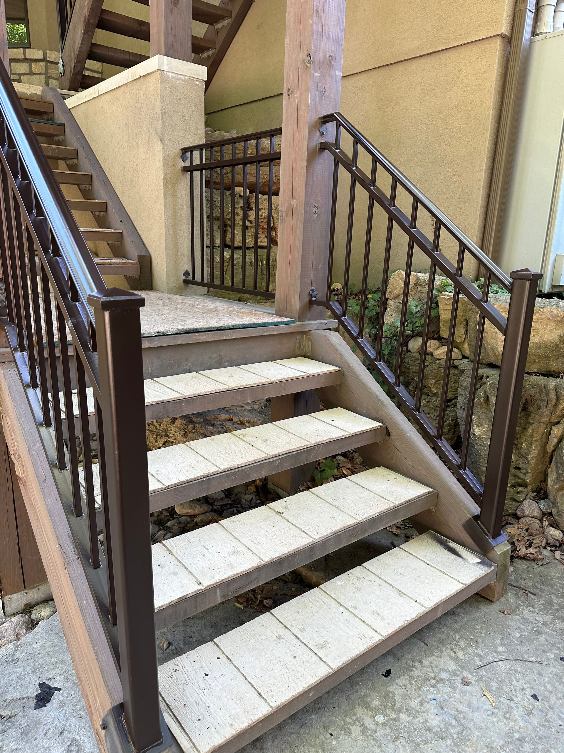 Brown outdoor stairs with railings leading to a gate on a stucco building.