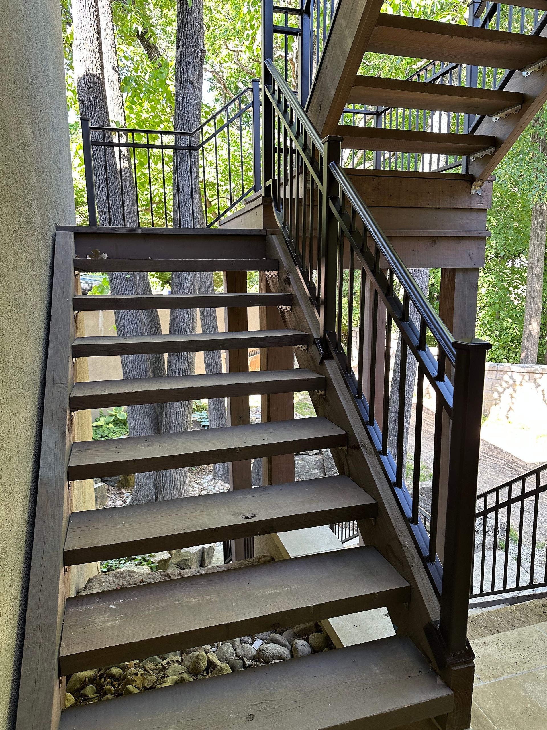 Outdoor wooden stairs with black metal railing.