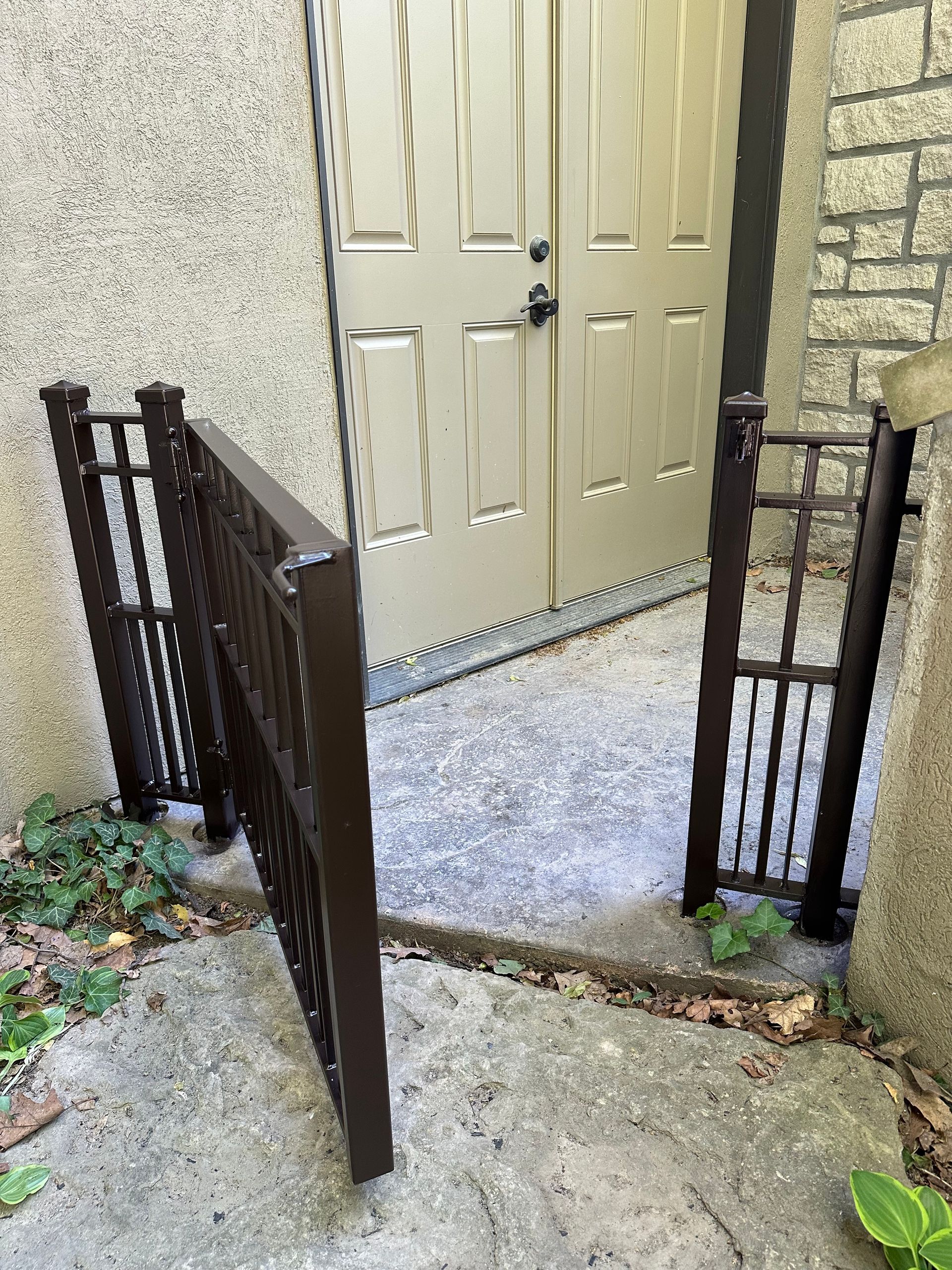 Brown metal railing forming a gate around a concrete entry to a beige door.