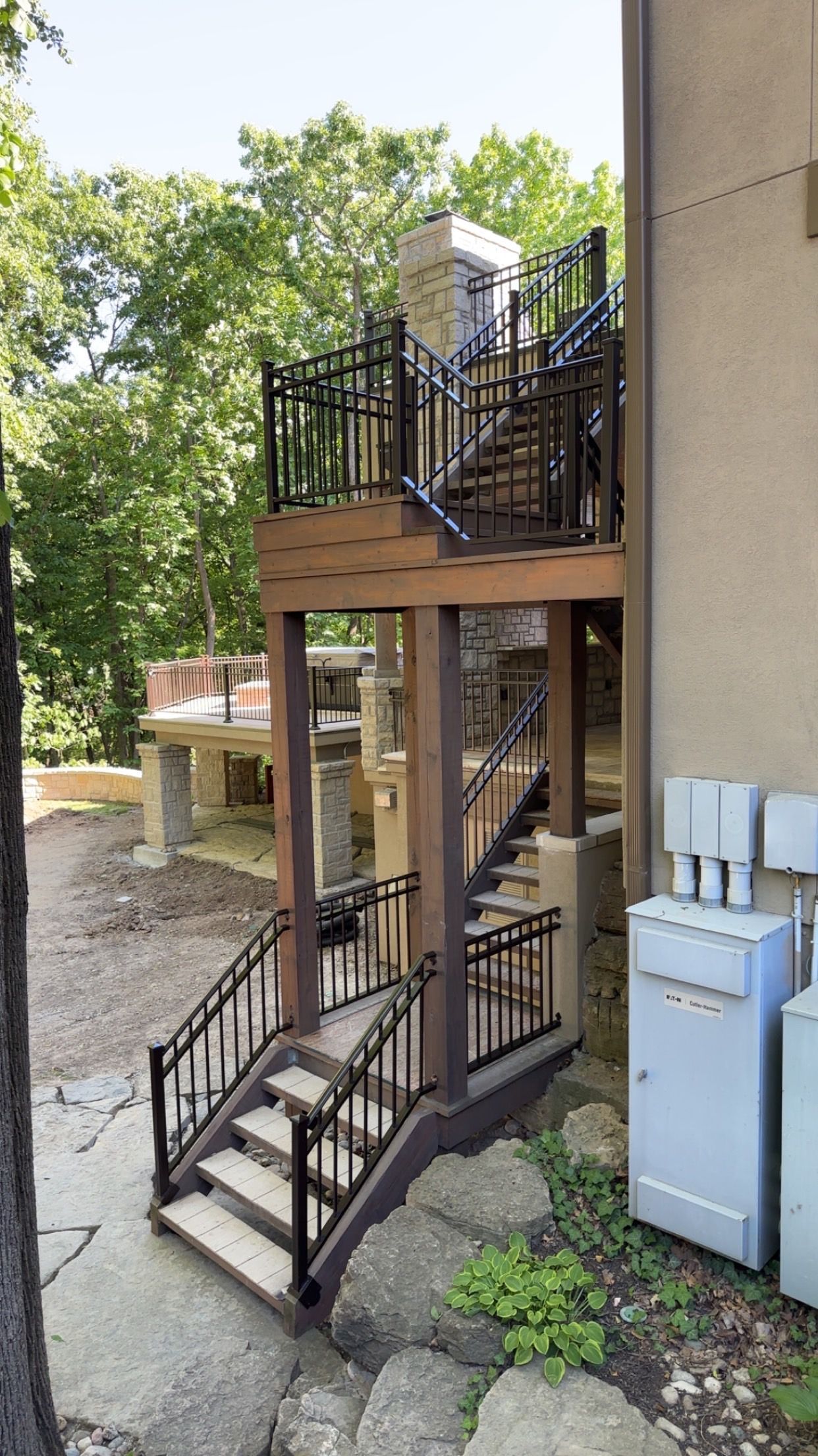 Outdoor staircase with brown wooden framing, black metal railings, leading to a deck.