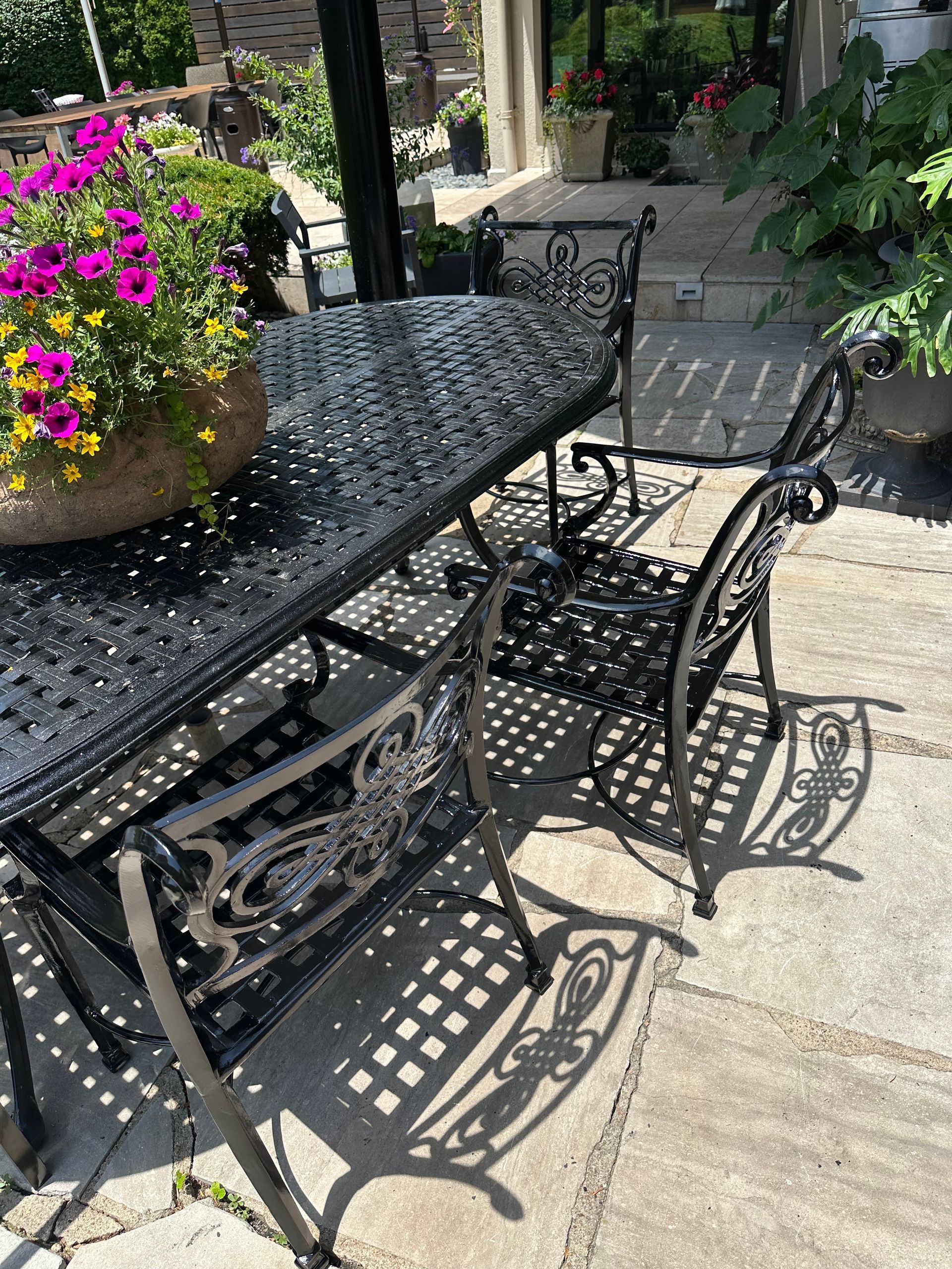 Black ornate patio table and chairs with a flower pot on the table.