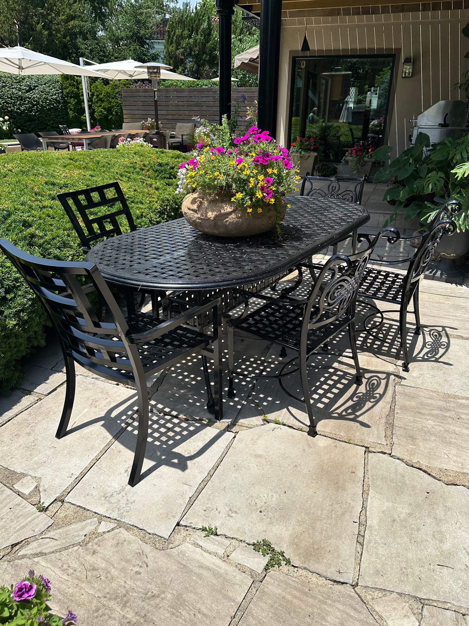 Outdoor patio dining set with black metal table and chairs, potted flowers.