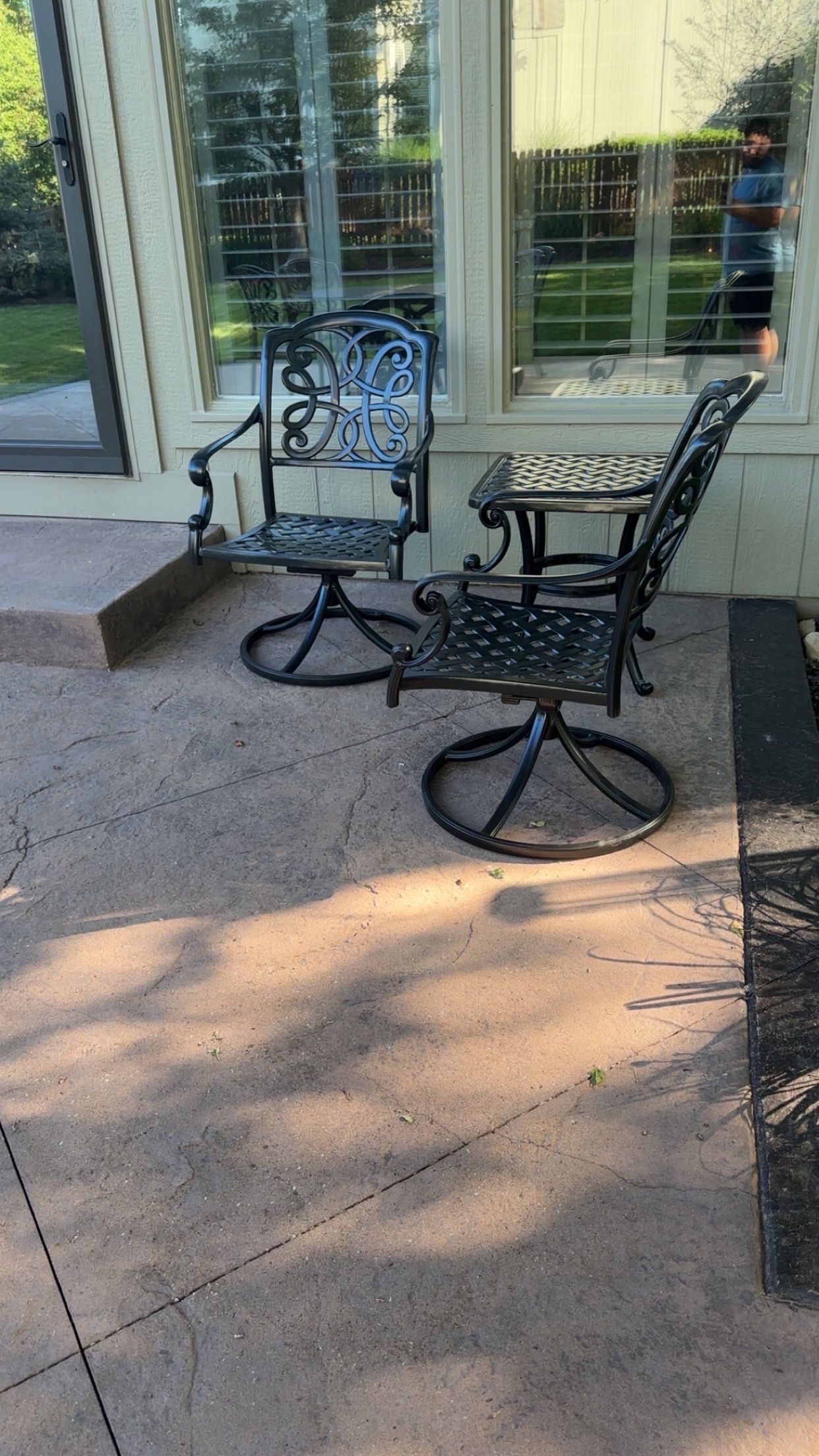 Two black wrought iron chairs and a small table on a concrete patio.