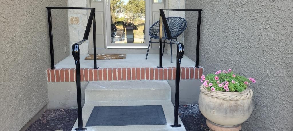 A black wrought iron railing surrounds a brick and concrete entryway with a potted plant to the side.