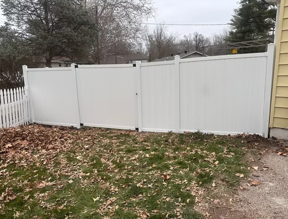White vinyl fence in a yard with leaves.