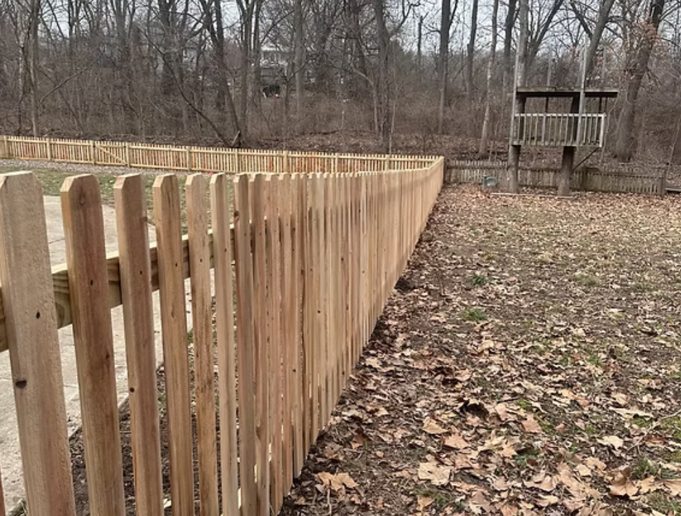 Wooden picket fence in a yard with fall leaves; a treehouse is in the background.