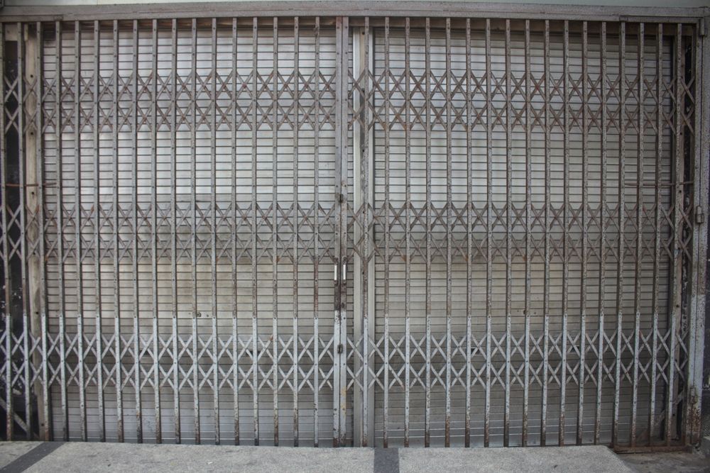 Gravel yard with a stone retaining wall, wooden fence, and a wheelbarrow next to a building.