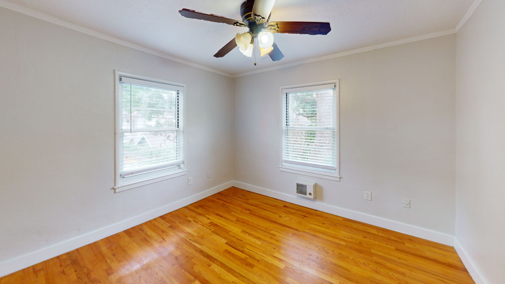 An empty bedroom with hardwood floors and a ceiling fan.