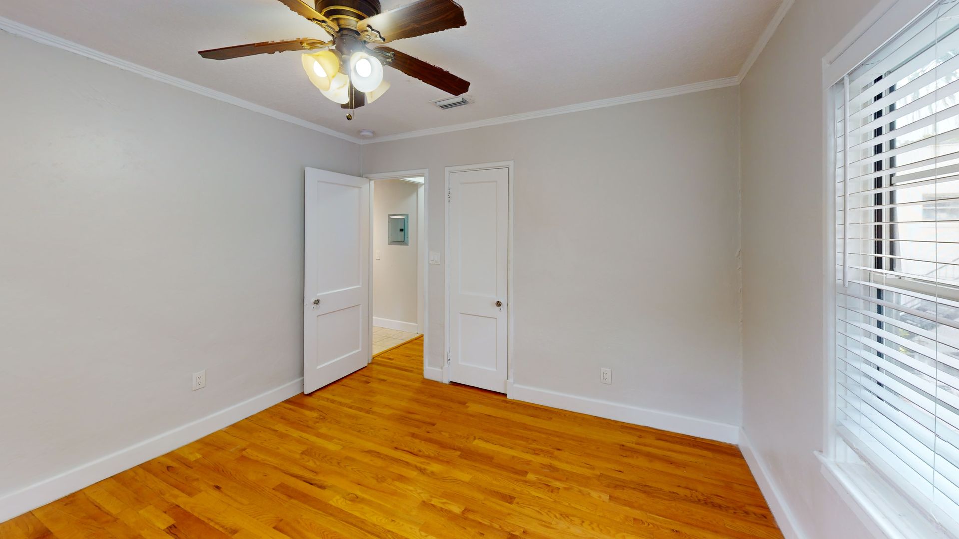 An empty bedroom with hardwood floors and a ceiling fan.