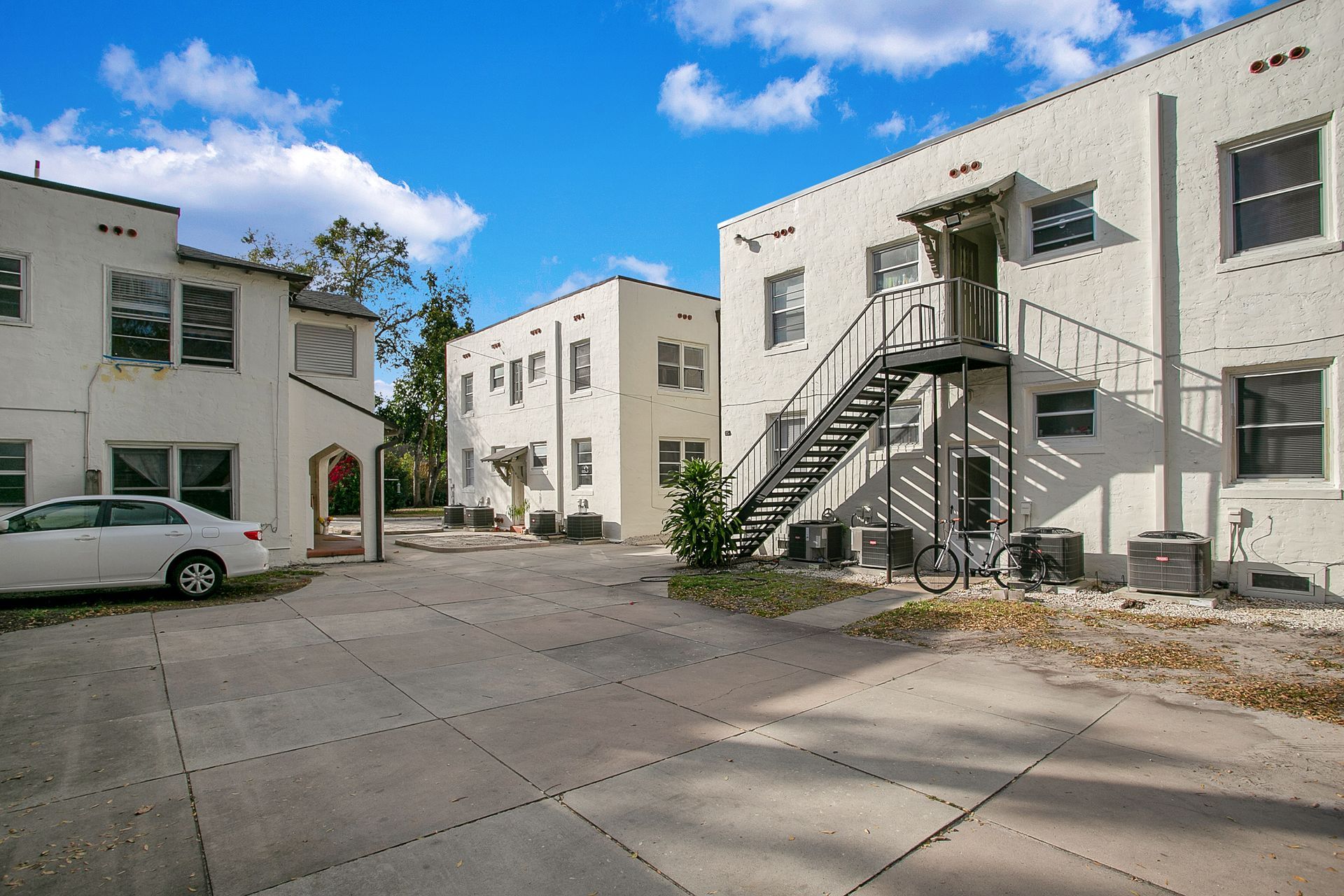 A white car is parked in front of a building with stairs.