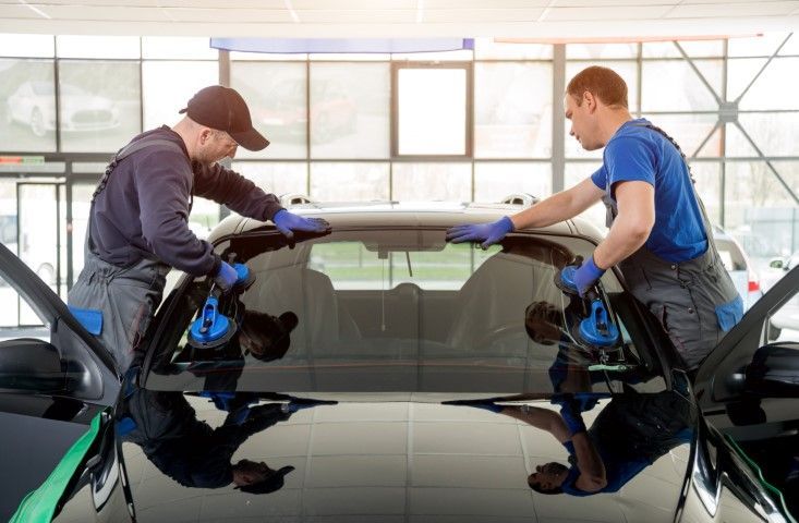 Two workers in blue shirts and gloves polishing a black car in a bright auto shop