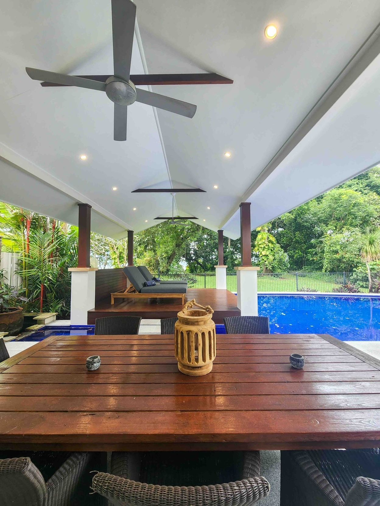 A Wooden Table and Chairs Under a Ceiling Fan Next to a Swimming Pool — Leemark Design Services In Parramatta Park, QLD