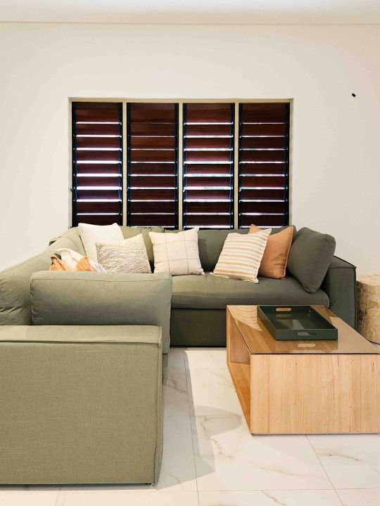 A Living Room With a Couch, Chair, Coffee Table and Shutters on the Windows — Leemark Design Services In Parramatta Park, QLD