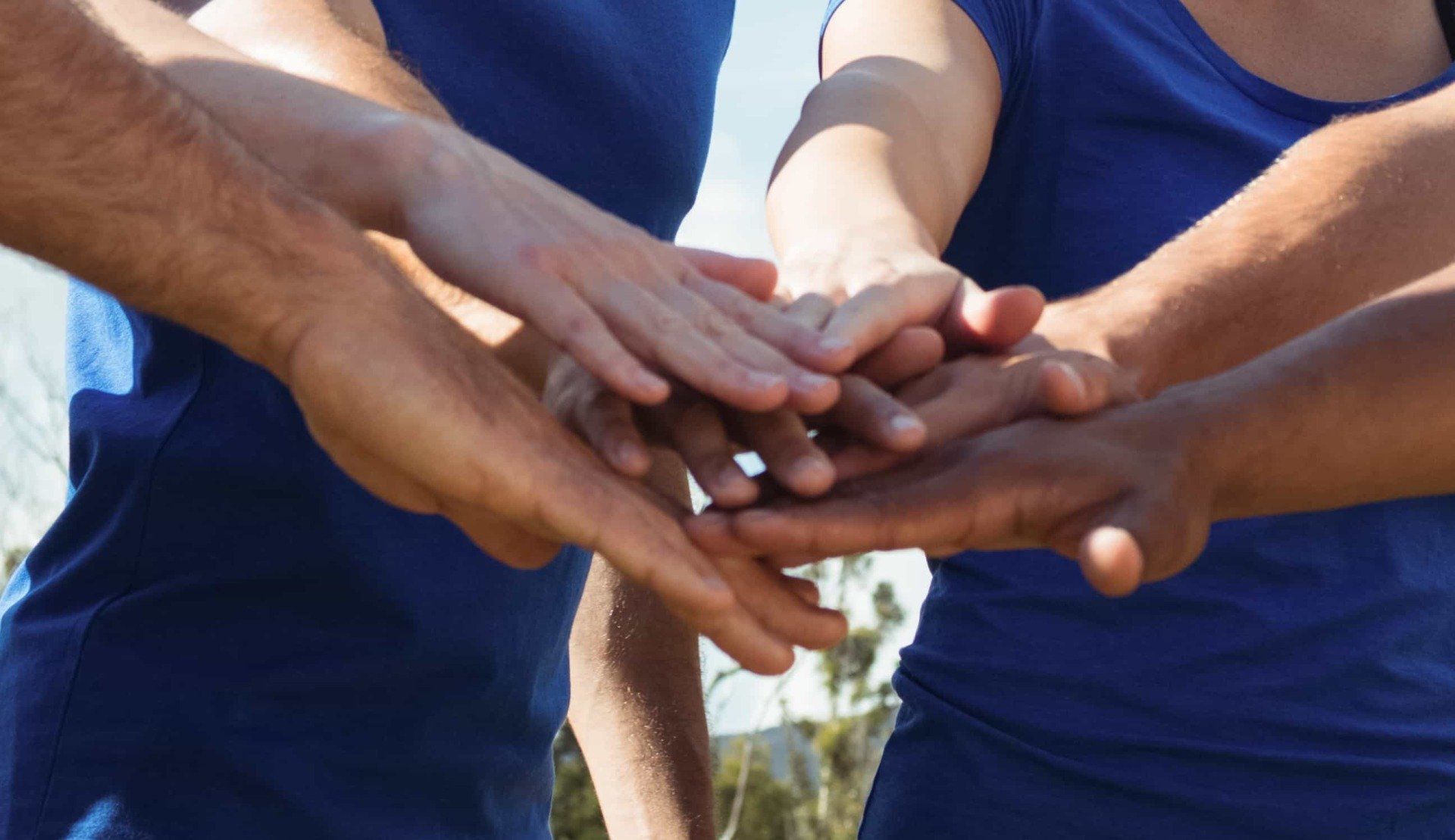 Mani unite in un capannello di squadra, sullo sfondo si vedono le magliette blu.