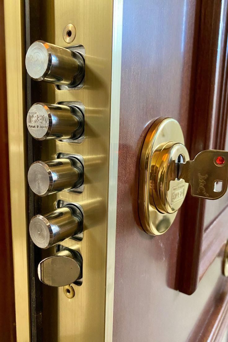 Cerradura de seguridad dorada con llave insertada, mostrando varios cerrojos extendidos. Puerta marrón.